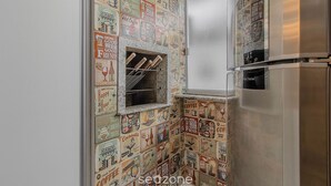 A kitchen with a stainless steel refrigerator, a built-in wine rack, and a backsplash with vintage-style drink-related illustrations. - RAL - Apartamentos Cerca de Duna y Praia dos Ingleses (Florianópolis)