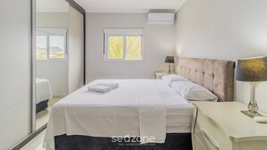 A modern bedroom with a large bed, bedside tables, a window, and an air conditioning unit. - RAL - Apartamentos Cerca de Duna y Praia dos Ingleses (Florianópolis)