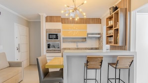 A compact kitchen with a central island, built-in appliances, and a wooden cabinet with glassware. - RAL - Apartamentos Cerca de Duna y Praia dos Ingleses (Florianópolis)