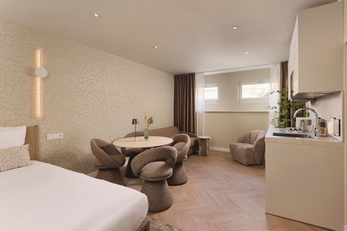 A modern hotel room with a bed, a round dining table, and two chairs.
