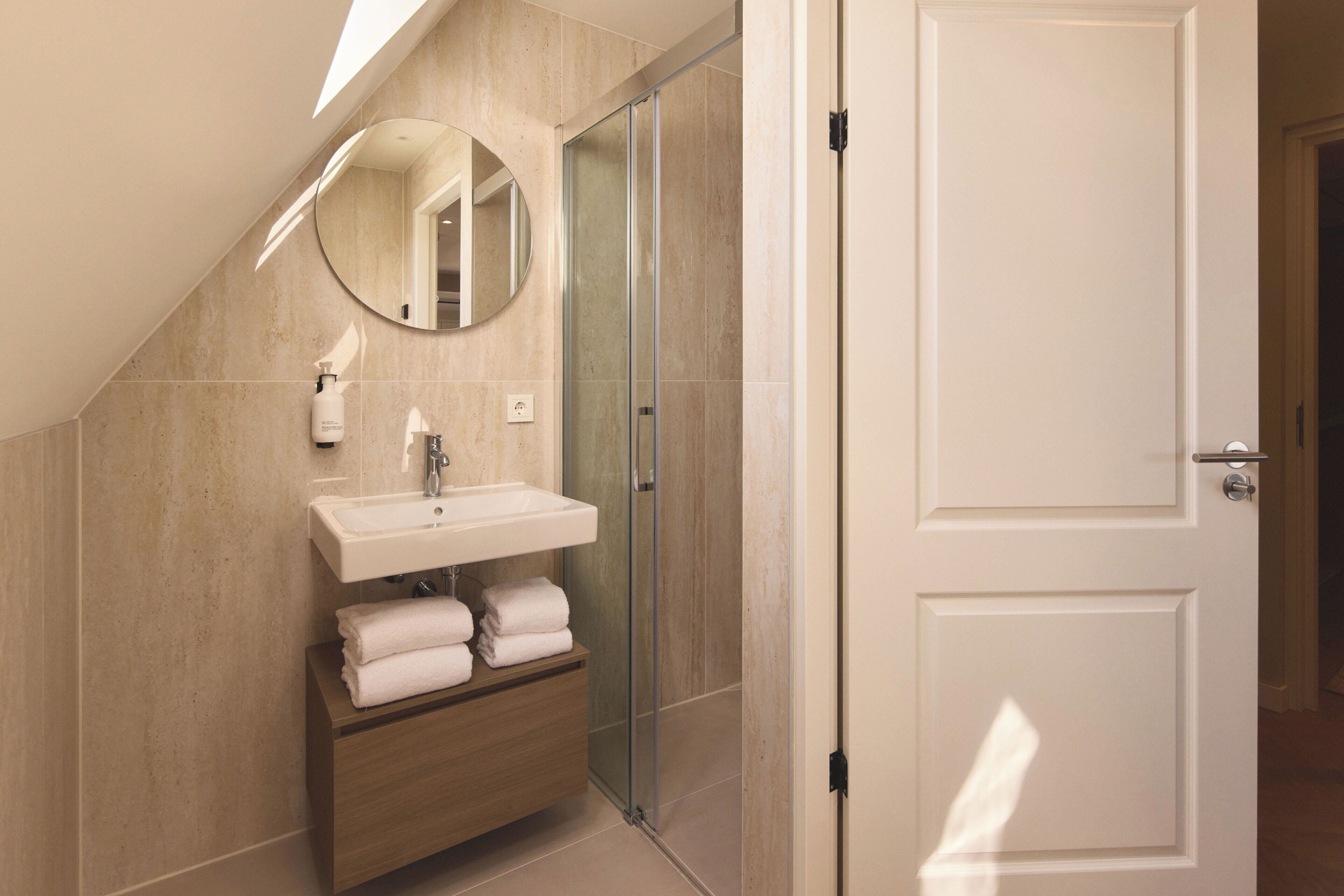 Une salle de bain moderne avec une douche à parois de verre, un lavabo avec un miroir et un meuble-lavabo en bois agrémenté de serviettes.