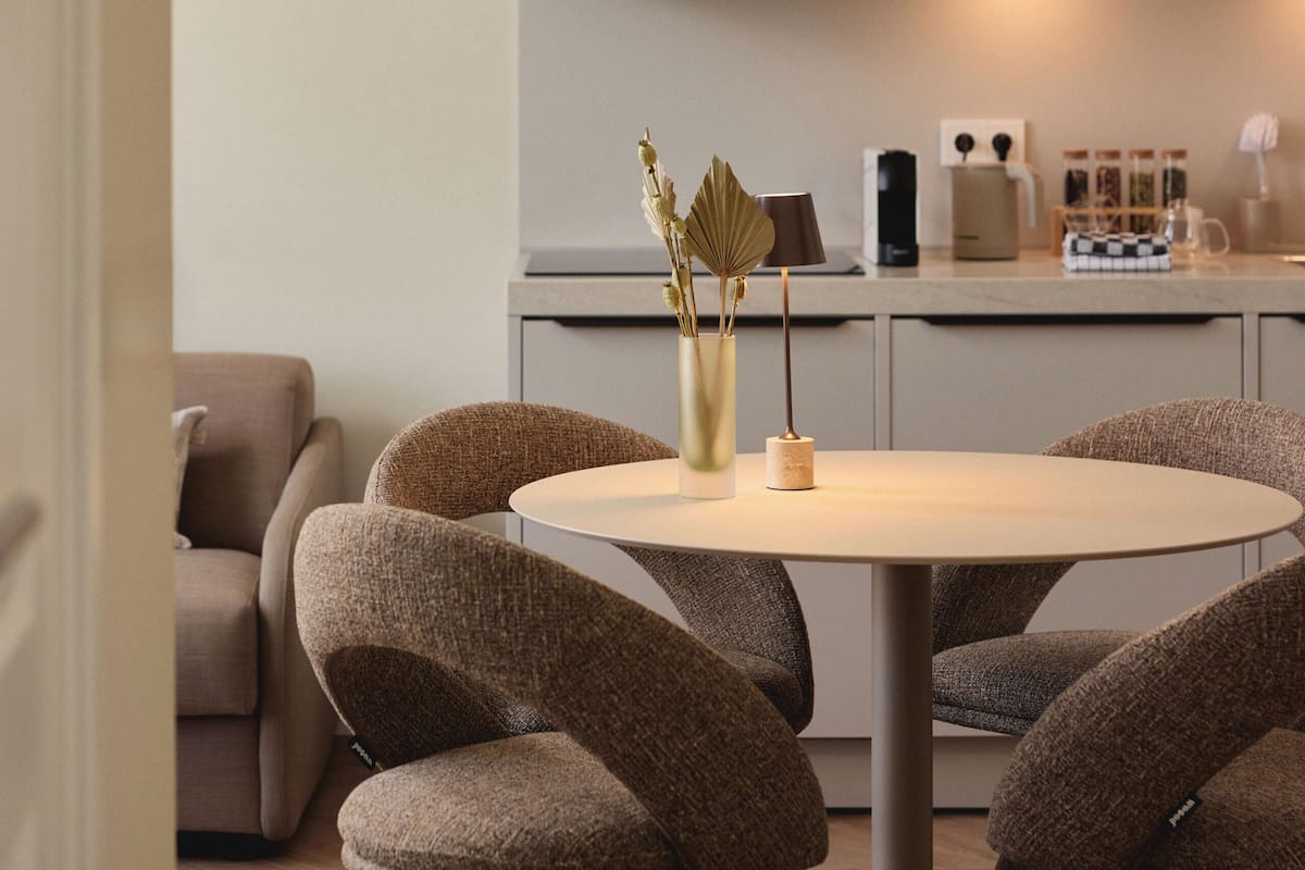 A modern kitchen with a microwave, coffee maker, and a dining area with a round table and cushioned chairs.