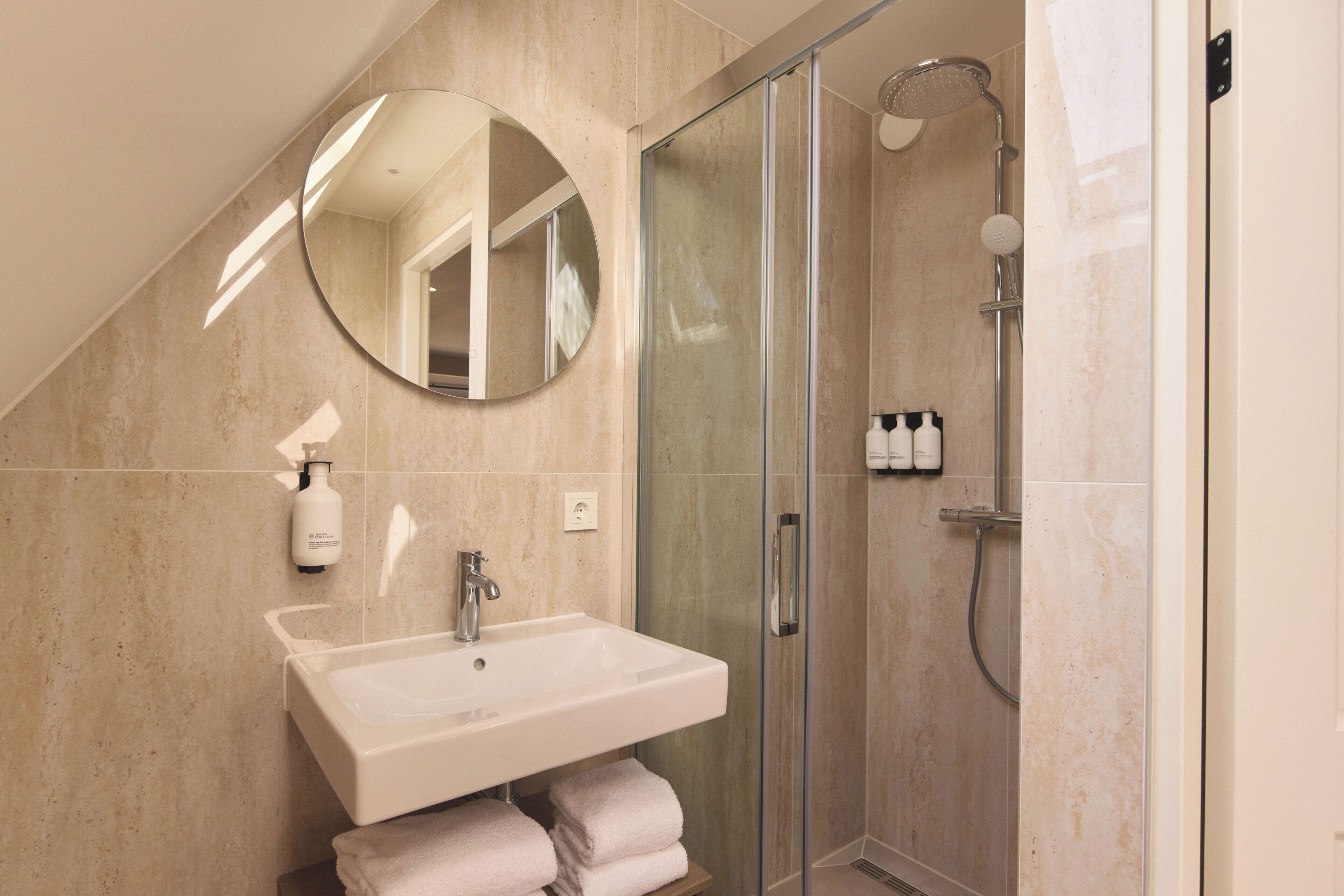 Une salle de bain moderne avec une douche à parois de verre, un lavabo avec un miroir au-dessus et des serviettes soigneusement pliées.