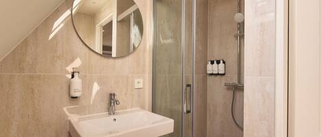 Une salle de bain moderne avec une douche à parois de verre, un lavabo avec un miroir au-dessus et des serviettes soigneusement pliées.