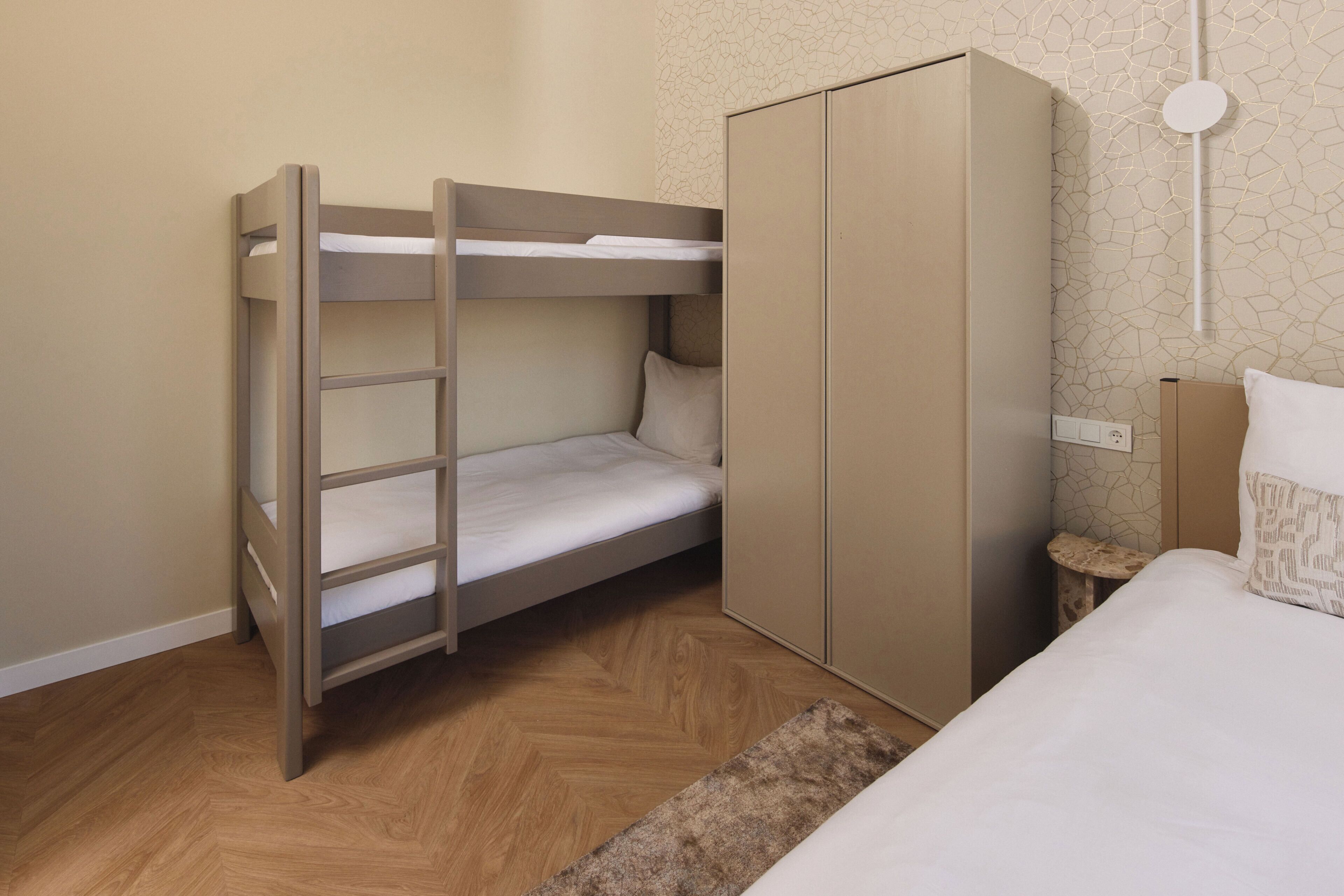 Een stapelbed met een onderbed, een kledingkast, een nachtkastje en een bed met kussens.