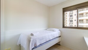 Une petite pièce propre, avec un lit simple, une fenêtre donnant sur un immeuble et un mur blanc.