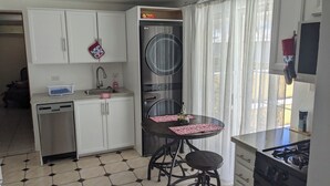 A compact kitchen with a dishwasher, a sink, a stove, and a dining area with a table and chairs. - Sweet Dreams by the Pool - V (Smiths)