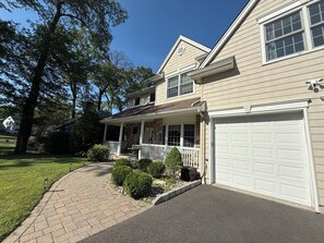 A two-story house with a covered porch, a stone facade, and a white garage door. - NEW" Cozy pristine home in Union County NJ, Mins to NYC free coffee, Smart Tvs (Mountainside)
