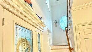 Un escalier avec des marches en bois et des murs blancs, menant à une porte dotée d’un vitrage et ornée d’une guirlande décorative.