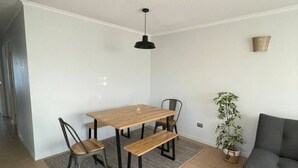 Un coin repas avec une table et des chaises en bois, un luminaire suspendu, un canapé gris et une plante en pot.