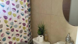 Une salle de bain comprenant des toilettes, un lavabo, un miroir et un rideau de douche orné d’un motif de feuilles.