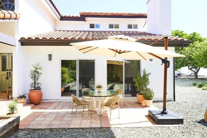 A patio with a glass table and chairs, a large umbrella, and potted plants.