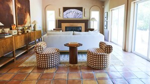 Une chambre spacieuse avec un grand lit, une cheminée et une vue sur l’extérieur. On y trouve deux tables rondes et deux chaises assorties, placées devant le lit.