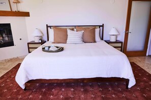 A neatly made bed with a white bedspread and brown pillows, two bedside lamps, and a small tray with a cup and a book on the nightstand.
