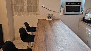 Een keuken met een houten tafel, zwarte stoelen, een Samsung magnetron en een raam met uitzicht op een gebouw.