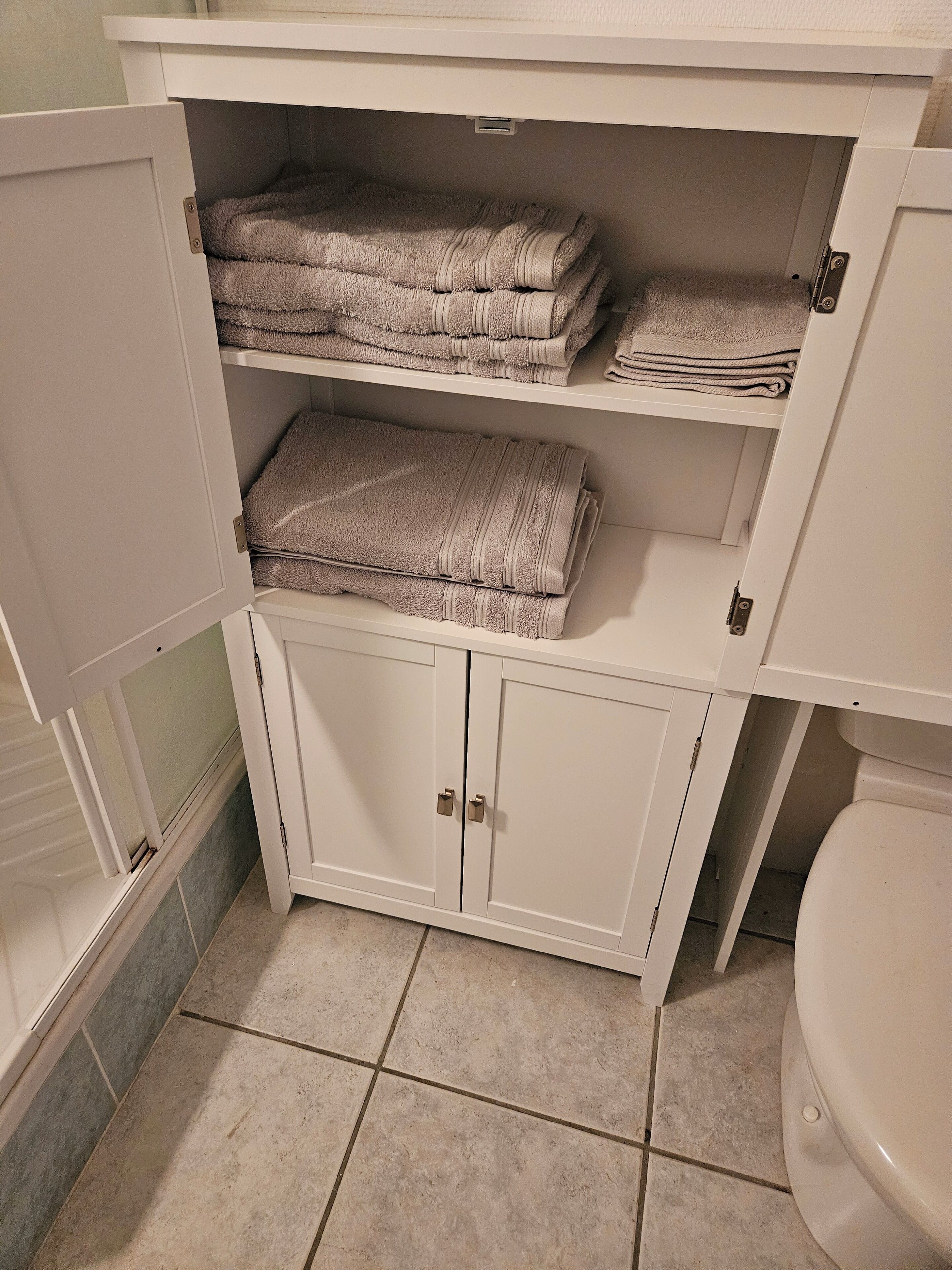 Une salle de bain avec un meuble blanc sous l’évier, dans lequel sont rangées des serviettes pliées.
