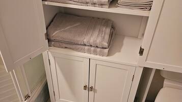 Une salle de bain avec un meuble blanc sous l’évier, dans lequel sont rangées des serviettes pliées.