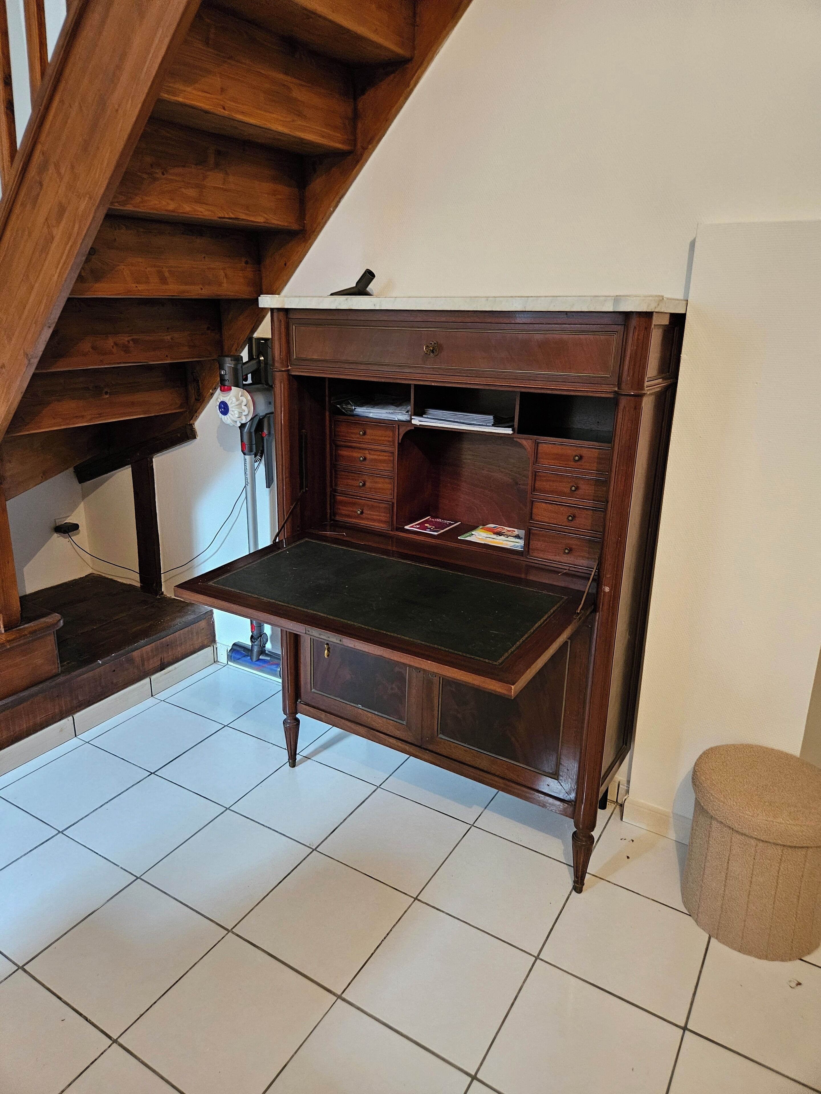 Escritorio de madera con cajones y estante, ubicado en una habitación con suelo de baldosas blancas y una escalera de madera.