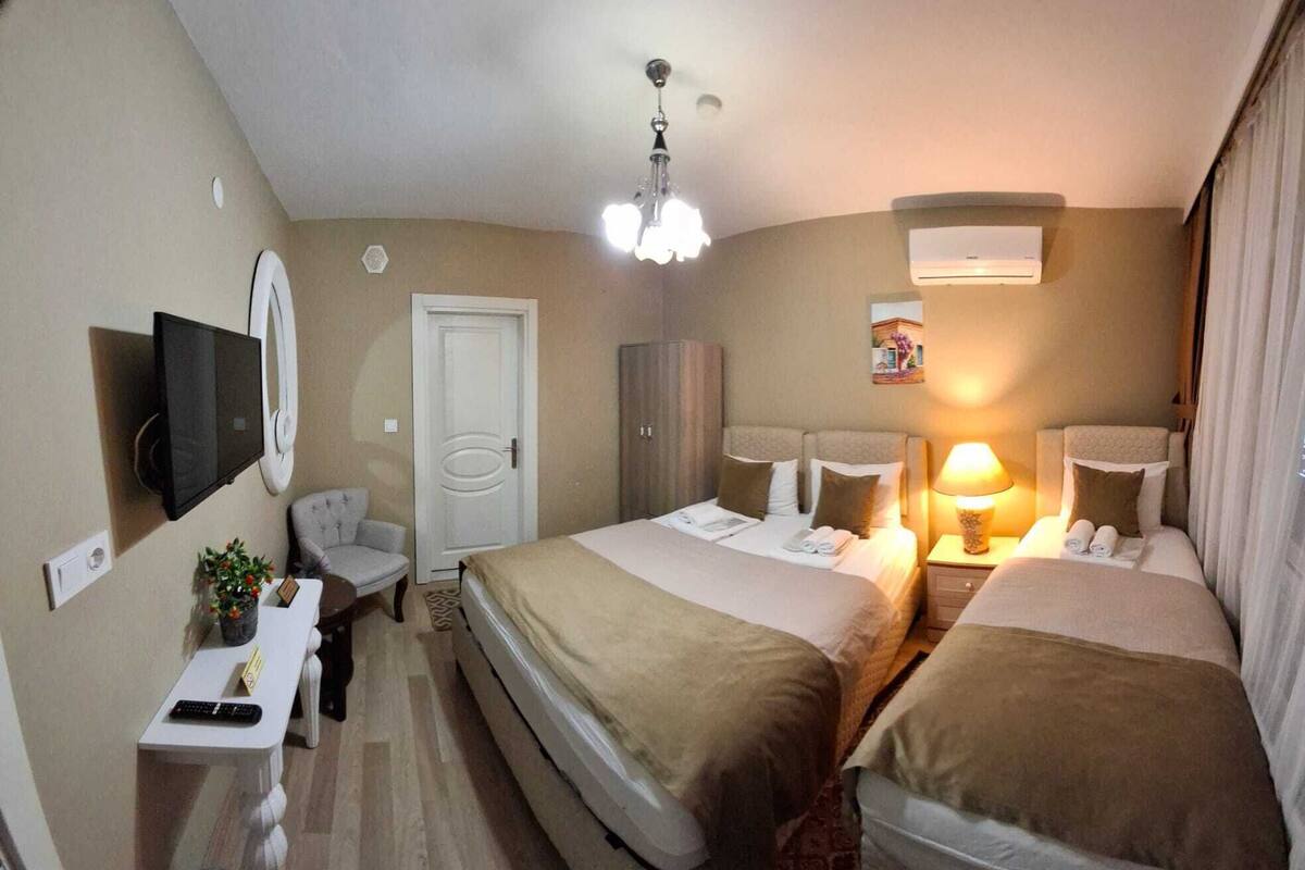 A hotel room with two beds, a TV, a desk with a remote, a chair, a wardrobe, and a ceiling light.