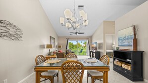 Zona pranzo con tavolo in vetro, sedie in vimini, lampadario e vista su un giardino tramite una porta scorrevole.