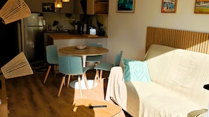 A modern living room with a sofa, chairs, a round table, and a kitchen area in the background. - LA ROSE DES SABLES - Near Beach (Les Sables-d´Olonne)