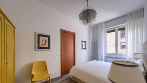 Een slaapkamer met een bed, een stoel, een lamp, een kroonluchter en een deur.