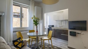 Een moderne woonkamer met een glazen eettafel, gele stoelen, een bank en een aan de muur bevestigde televisie.