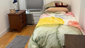 A bedroom with a bed, a nightstand, a radiator, a window with blinds, and a wooden floor. - Fully Furnished 1BR Apt Prime E 101st St Location, Steps from Central Park (New York)