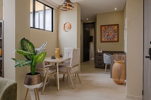 Un comedor con una mesa, sillas, una planta en maceta y un adorno en la pared.