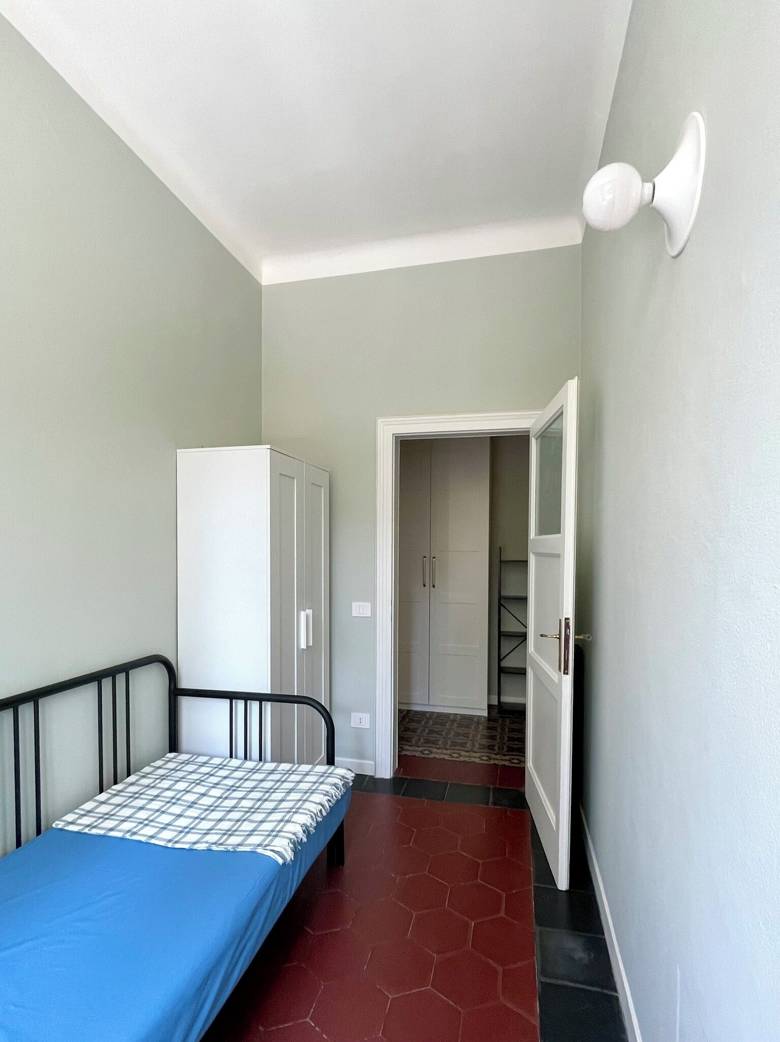 Un petit appartement d’une seule pièce comprenant un lit, une armoire et une porte donnant sur un couloir.