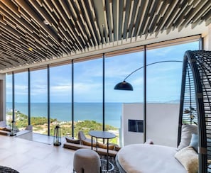 Una habitación moderna con ventanas amplias, techo con diseño geométrico, una mesa redonda y un sofá.