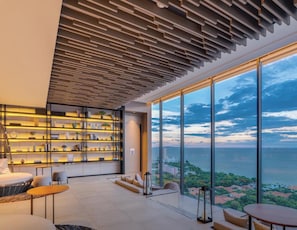 A modern interior with a large window overlooking a coastal view, a built-in bookshelf, and a seating area.