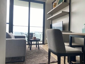 En moderne stue med sofa, spisebord og stole, et stort vindue med havudsigt og indbyggede reoler med pynteting.
