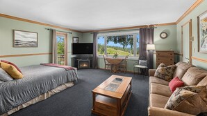 Un ambiente acogedor con cama, sofá, mesa de centro, televisión, chimenea, mesa de comedor y vistas al exterior.