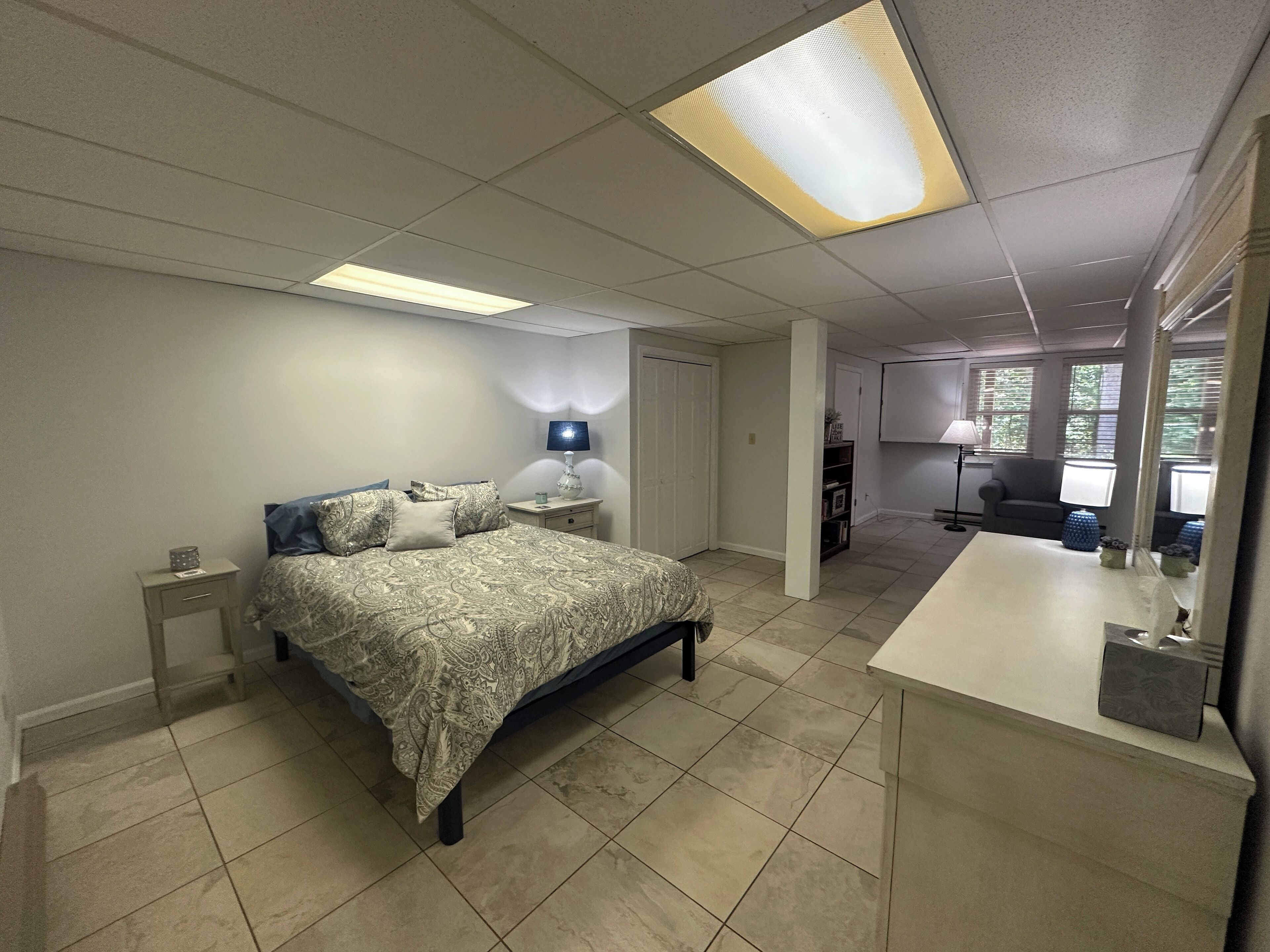 A bedroom with a bed, bedside tables, a lamp, and a view of a living area with a couch and a window.