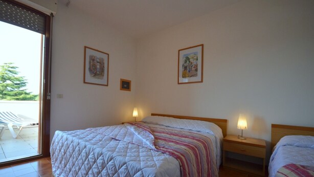 Une chambre avec deux lits, une porte-fenêtre coulissante donnant sur un balcon et deux lampes fixées au mur.