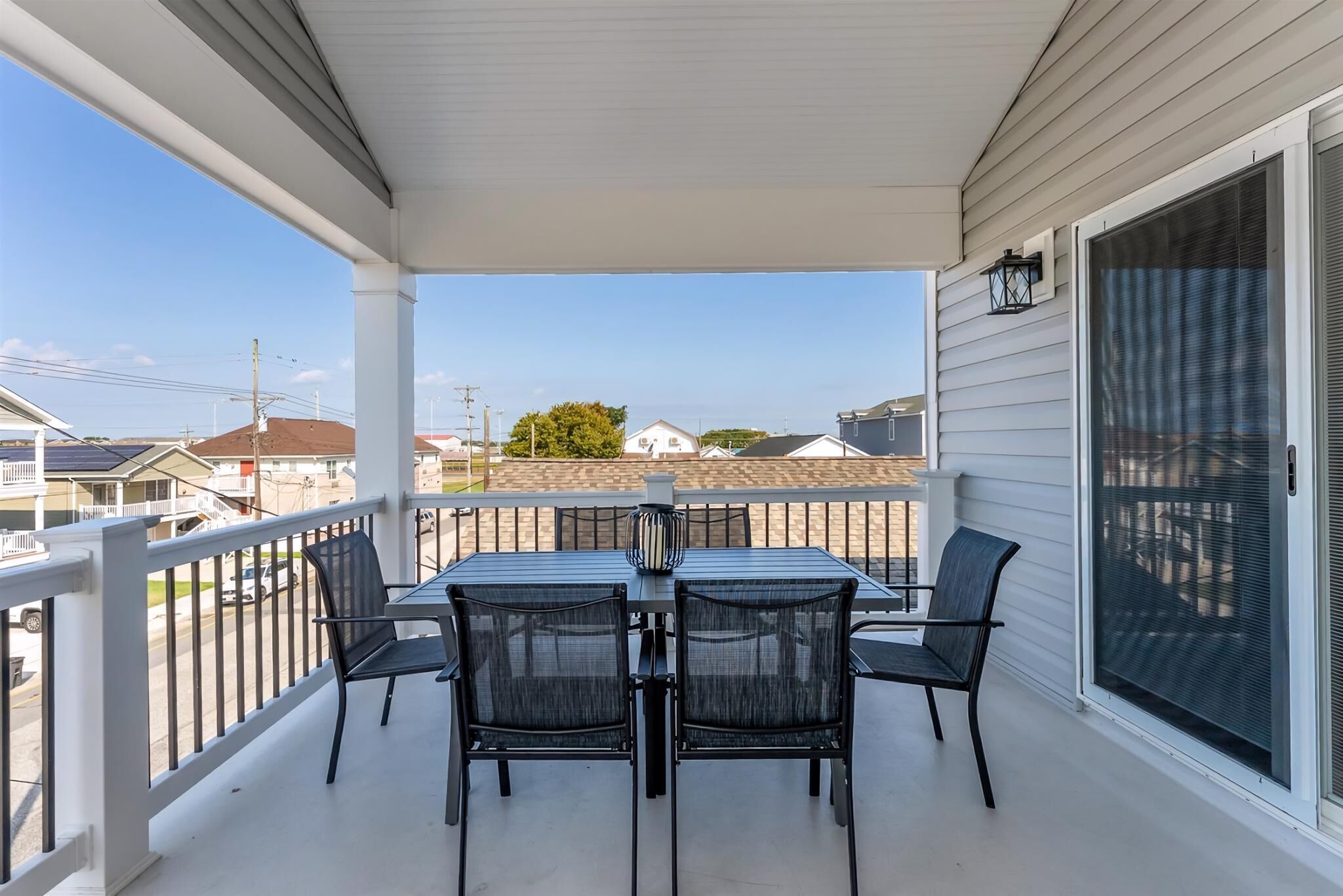 A covered patio with a table and chairs, a view of the neighborhood, and a large sliding glass door.
