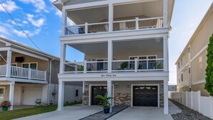A two-story residential building with a balcony on the upper floor, a garage at the ground level, and a small front yard with a potted plant. - Modern Beach Condo: Walk to Beach & Boardwalk (Wildwood)