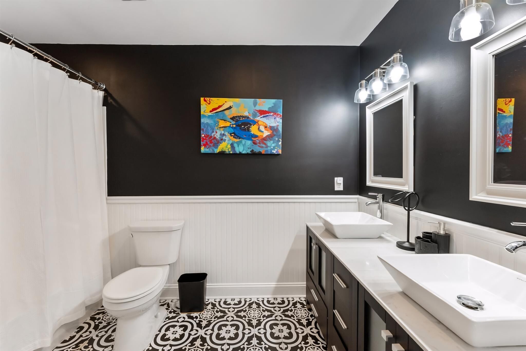 Ein modernes Badezimmer mit einem schwarz-weißen gemusterten Boden, weißen Sanitärobjekten und einem farbenfrohen Fischbild an der Wand.