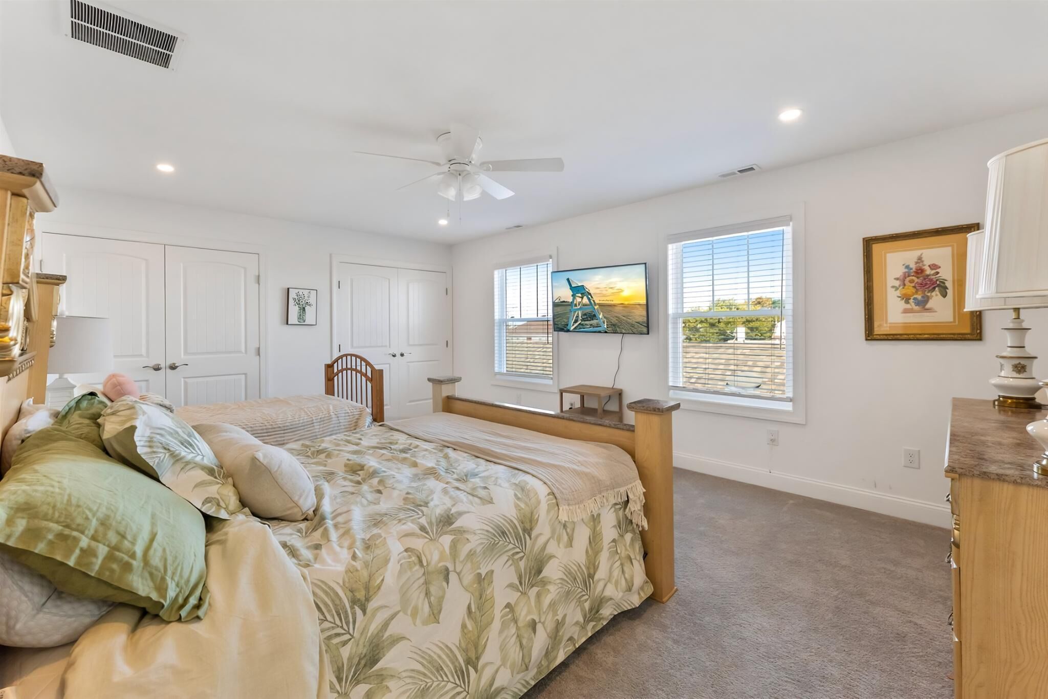 A bedroom with a bed, a ceiling fan, a TV, and a window with blinds.