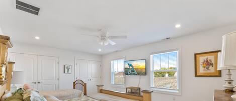 A bedroom with a bed, a ceiling fan, a TV, and a window with blinds.
