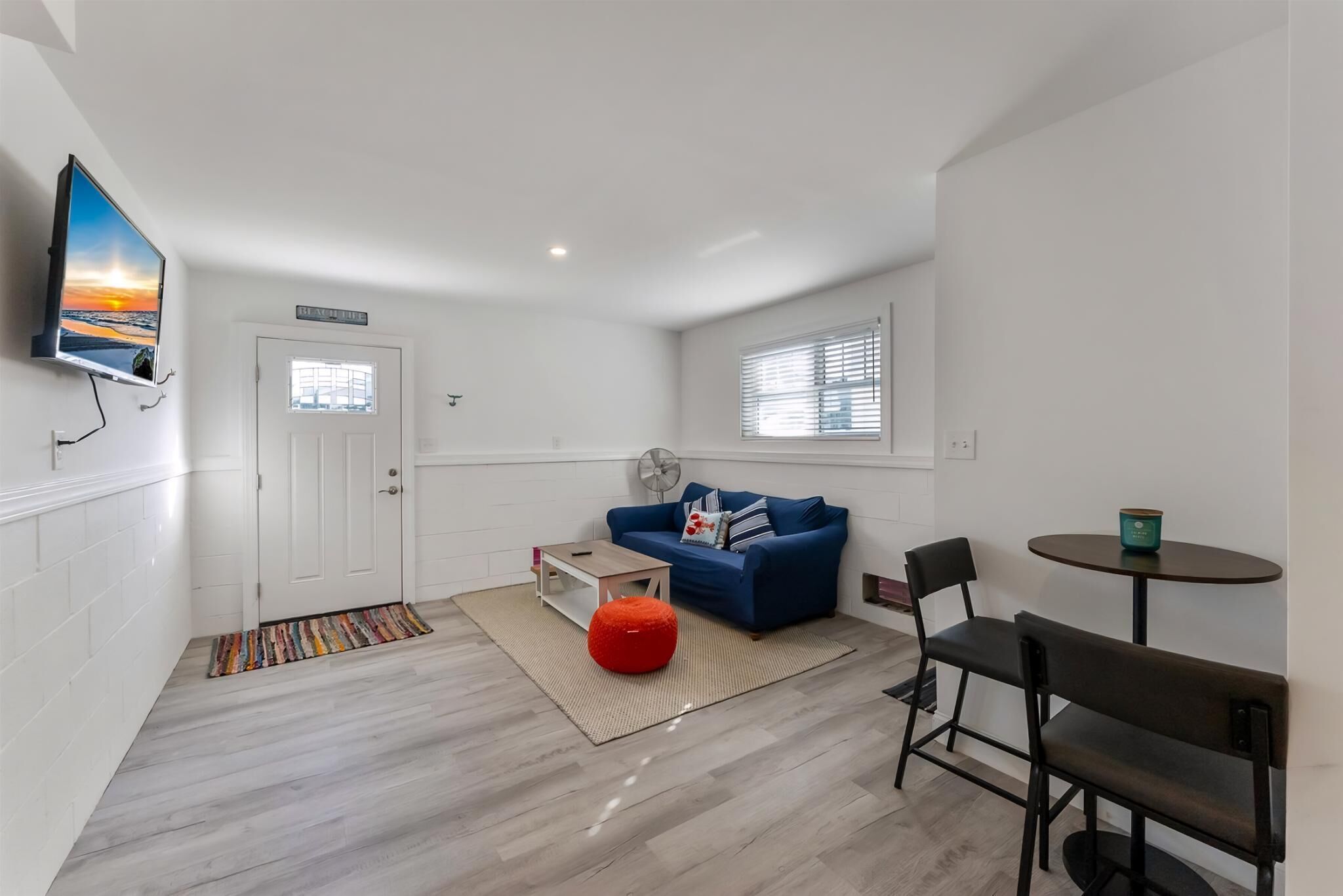 Ein modernes Wohnzimmer mit einem blauen Sofa, einem roten Hocker, einem Couchtisch und einem an der Wand befestigten Fernseher.