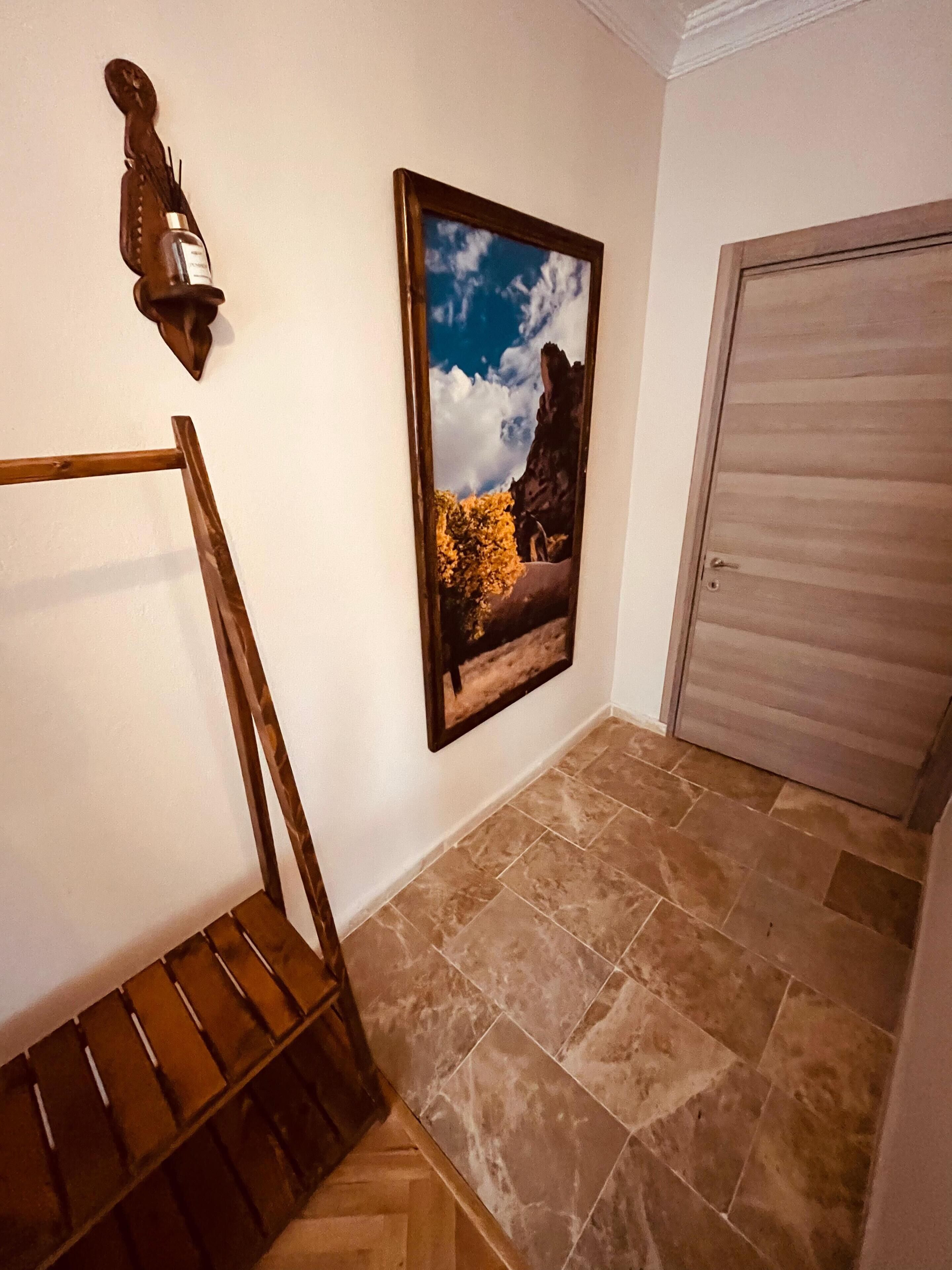 Un pasillo con un banco de madera, un cuadro enmarcado de un paisaje y una puerta.