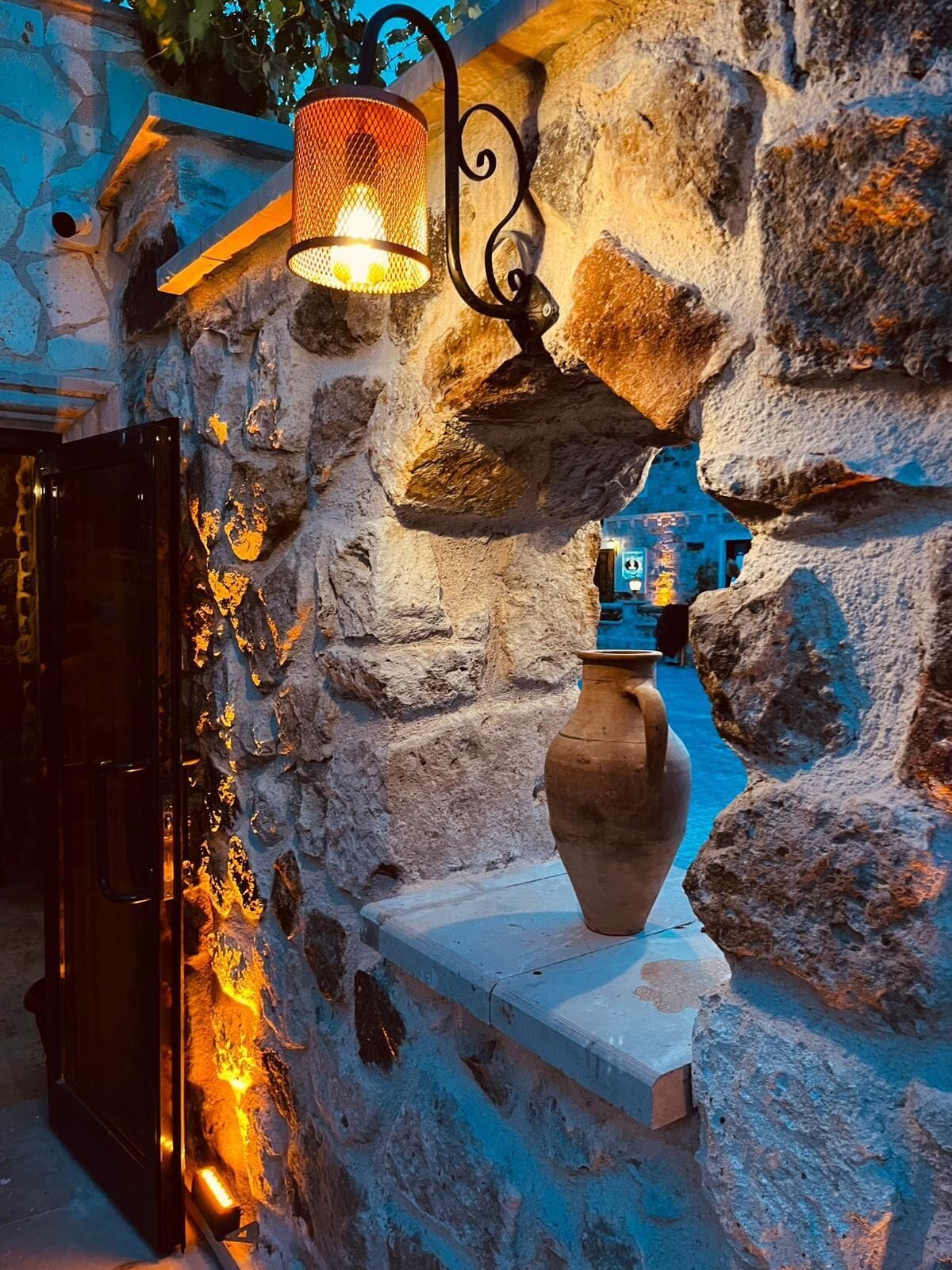A stone wall with a rustic lantern and a large clay pot.
