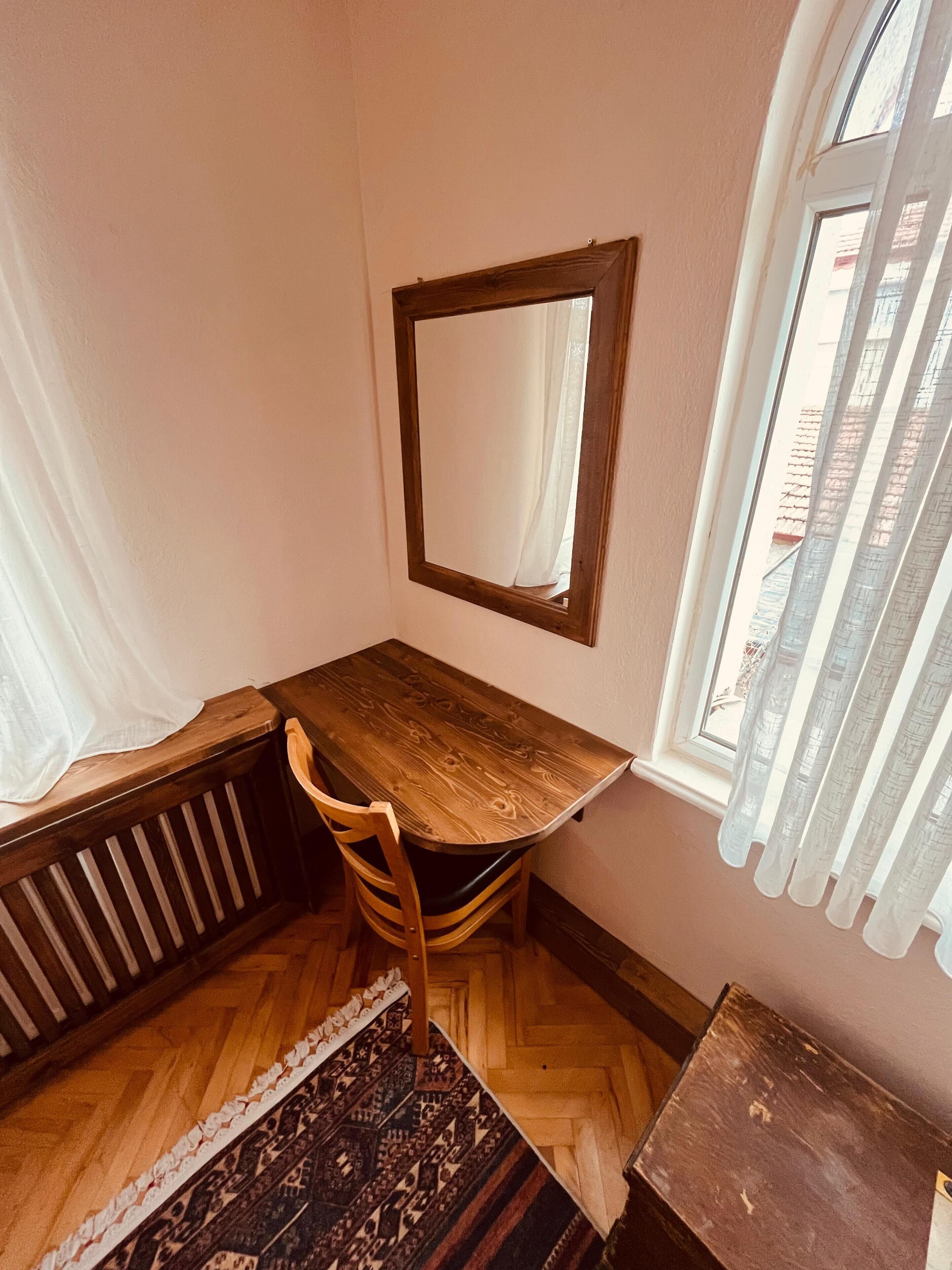 A corner room with a wooden desk, chair, and a large mirror on the wall.