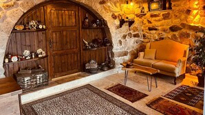 A rustic room with a stone wall, wooden door, shelves with clocks, a sofa, and a small table. - Cherrykonak cappadocia (Nevsehir)