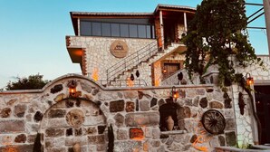 A stone building with a stone staircase, a sign reading "Cherry Konak Cappadocia," and a stone wall with a wheel and lanterns. - Cherrykonak cappadocia (Nevsehir)