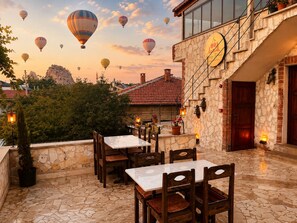 A patio with stone flooring, wooden tables and chairs, and a view of hot air balloons in the background.