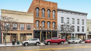 A row of buildings with a brick facade, a white building with a sign, and parked vehicles on the street. - Luxury Loft •Downtown • Full Kitchen • (Delaware)