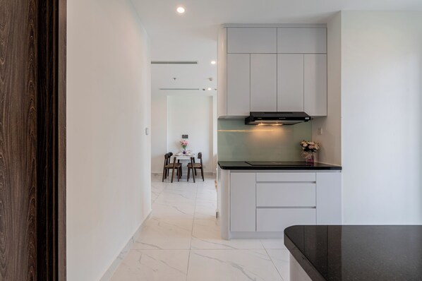 Una cocina moderna con armarios blancos, encimera negra y un comedor al fondo.